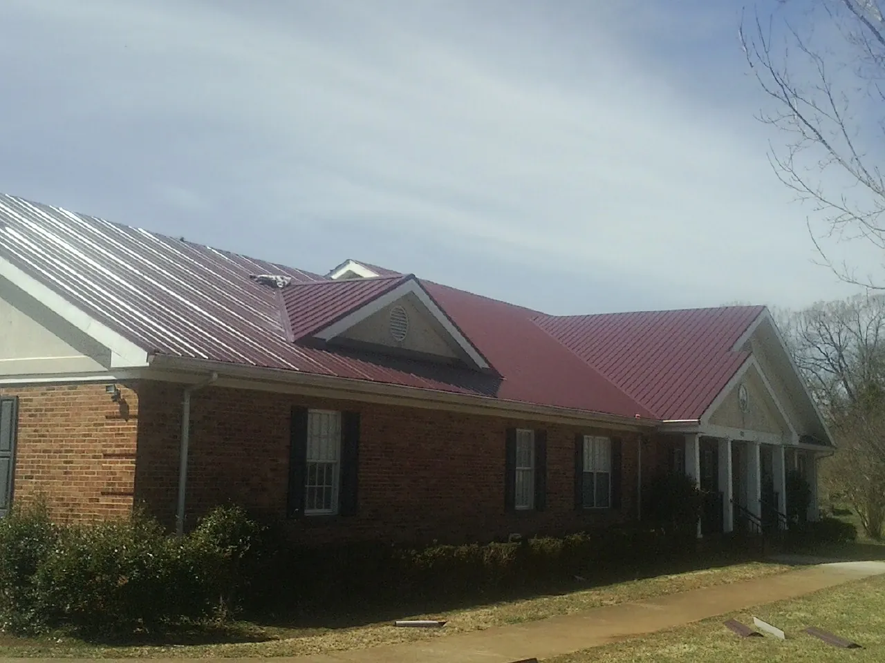 Red metal roof with gabled entries on a long brick building, from a Hail Damage Roof Repair job in Williston