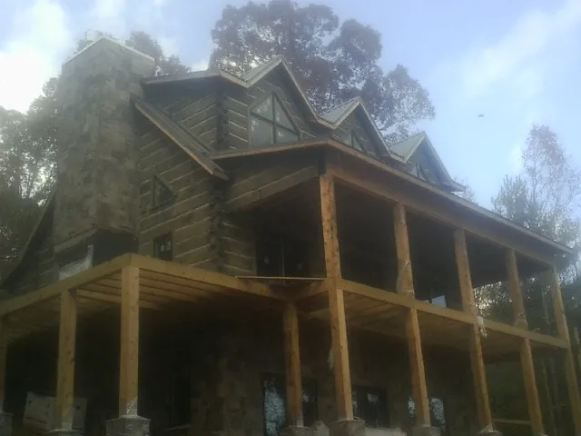 Stone chimney and dormers on a large log home with a timber porch in Williston